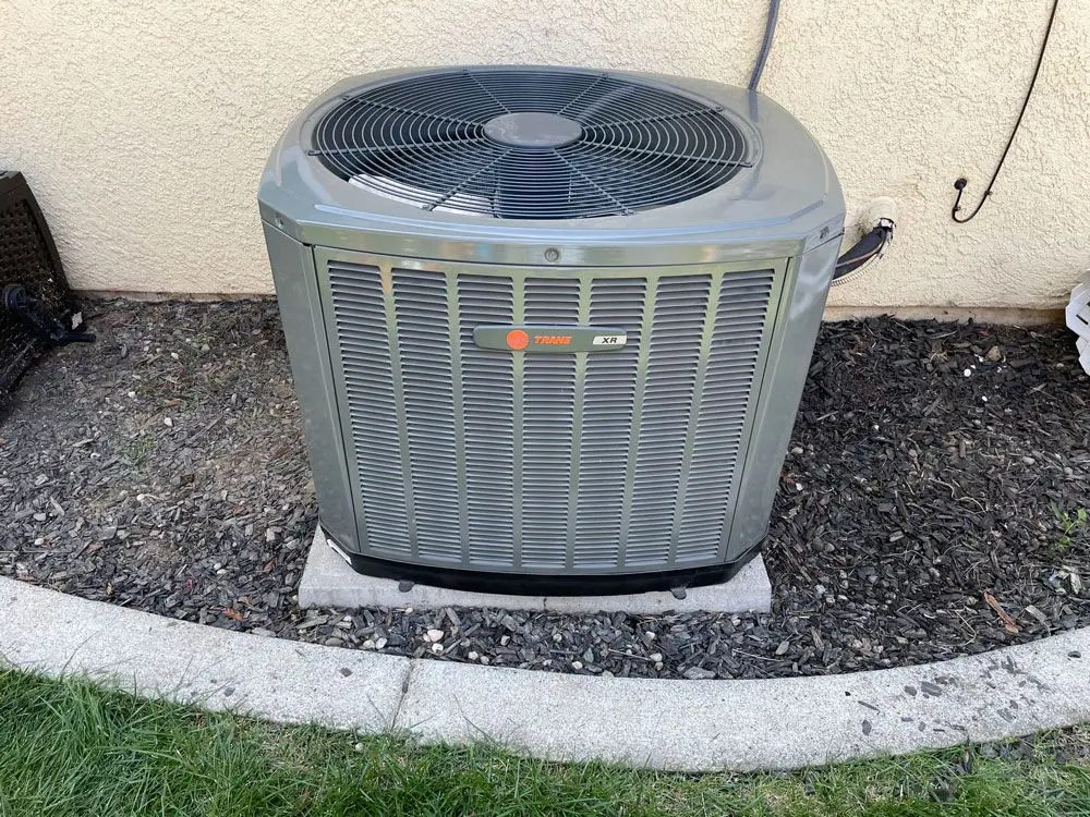 Trane XR air conditioning condenser unit installed on a concrete pad beside a stucco home