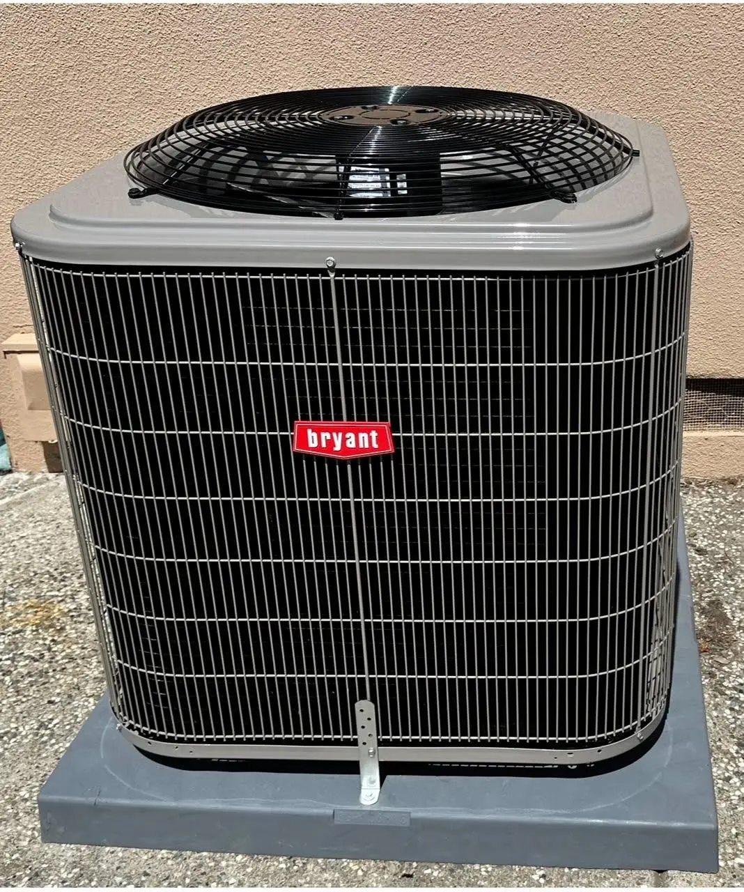 Bryant air conditioning condenser unit installed on a concrete pad beside a stucco wall
