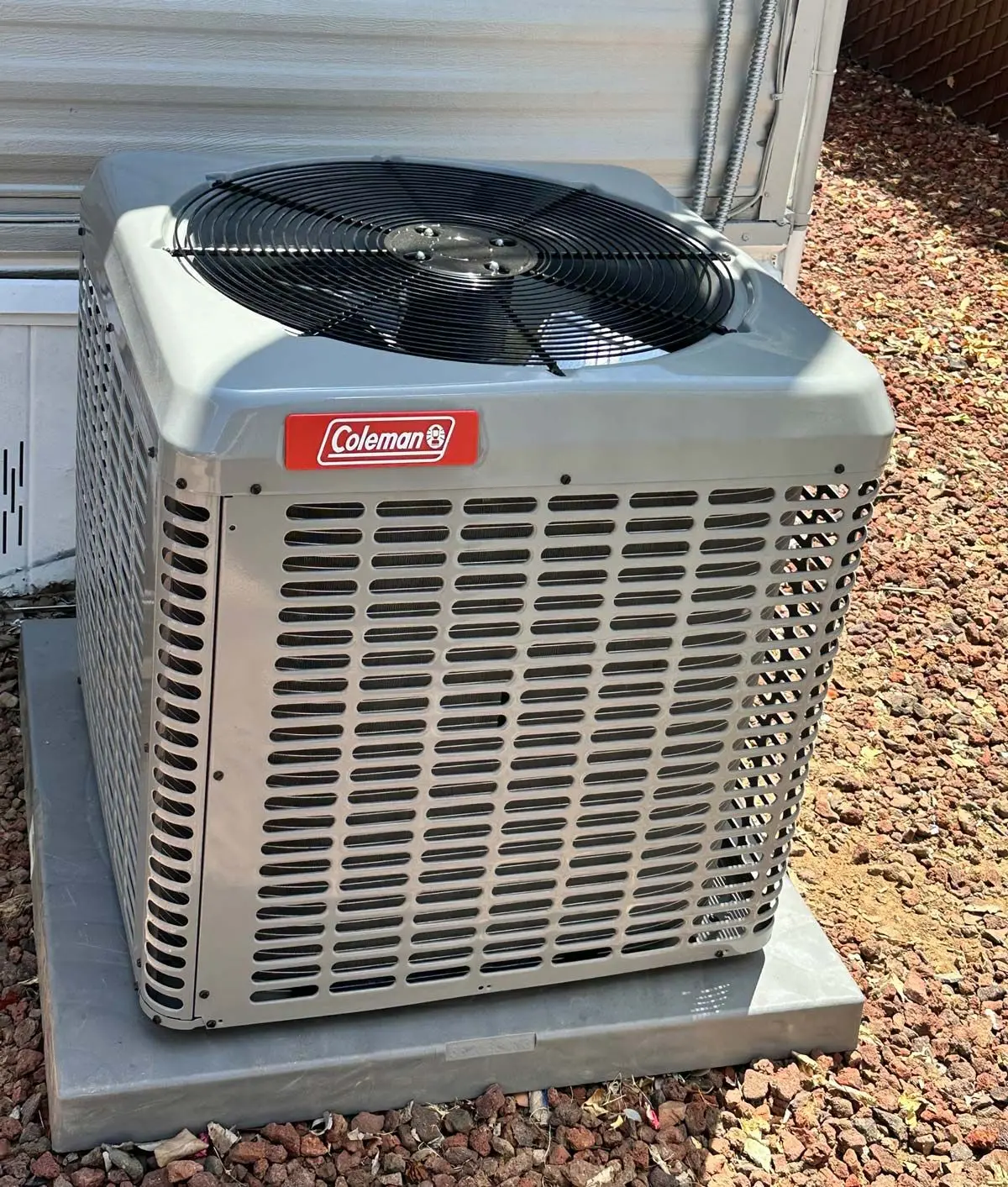 Coleman air conditioning condenser unit installed on a concrete pad beside a home