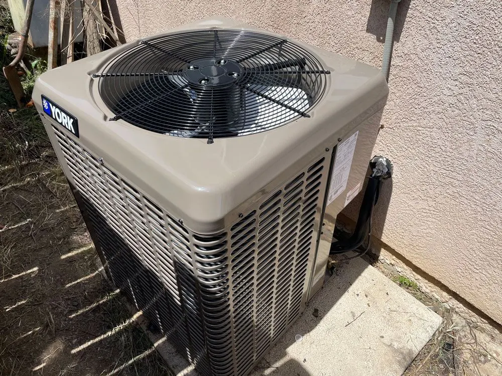 York outdoor air conditioning condenser unit installed on a concrete pad beside a stucco home